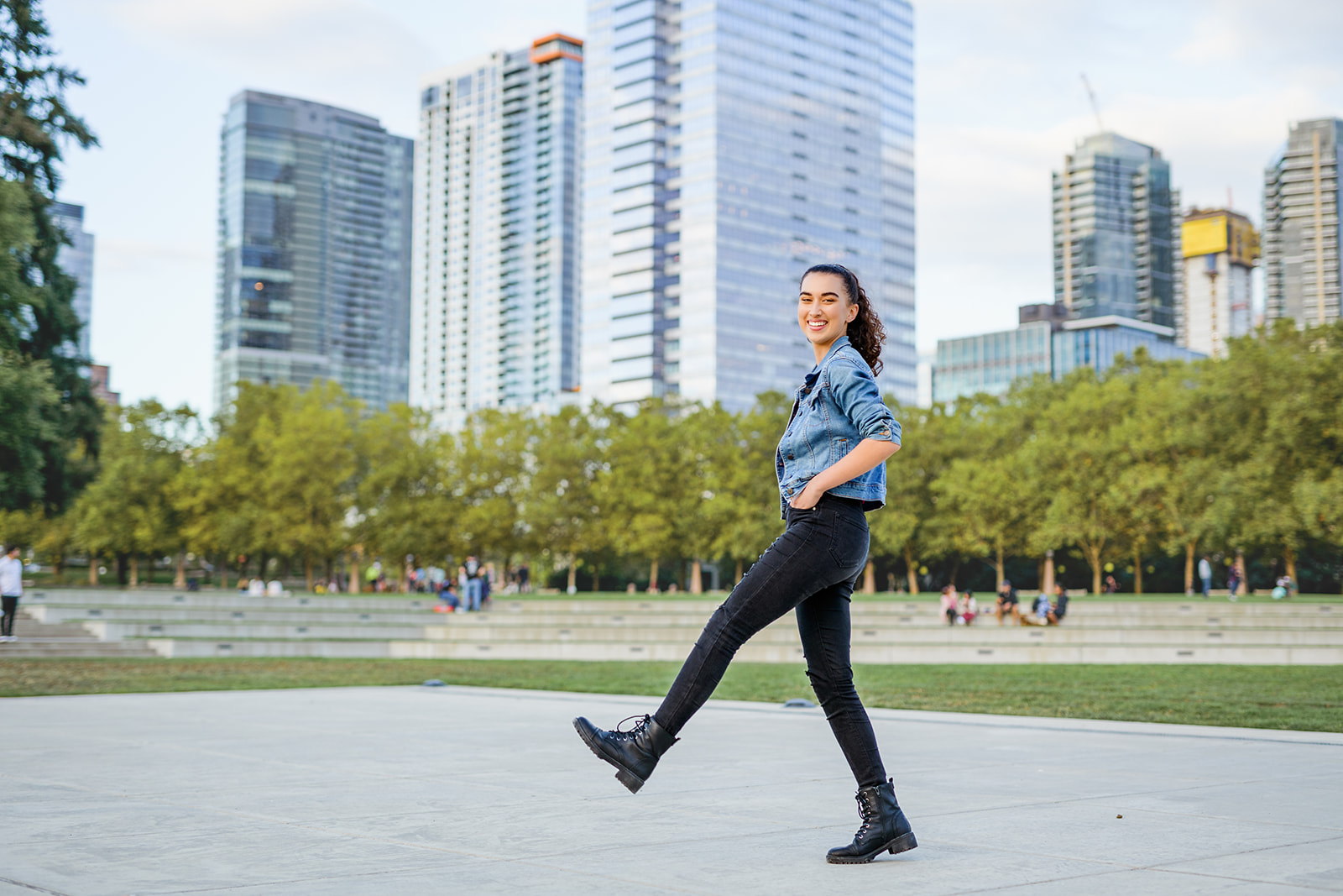 A high school senior plays and dances in a jean jacket and black pants in a metro park