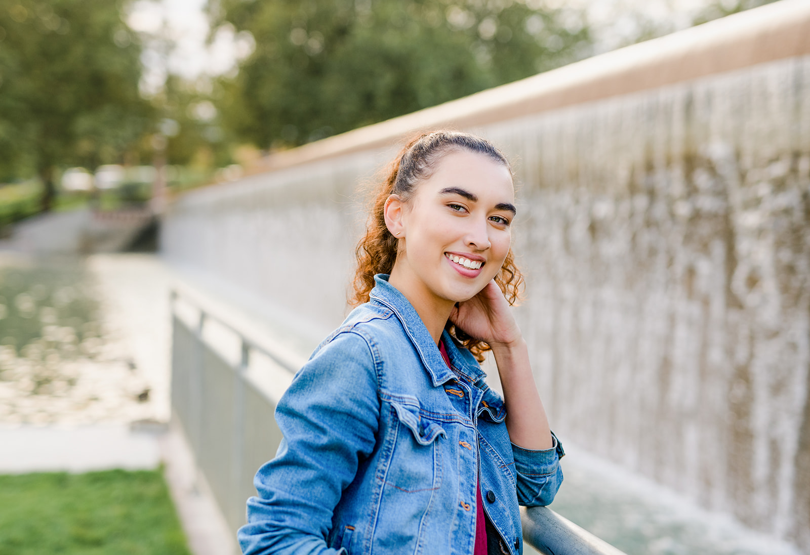 A high school senior in a denim jacket leans on a metal railing by a dam waterfall after visiting Colleges Near Seattle