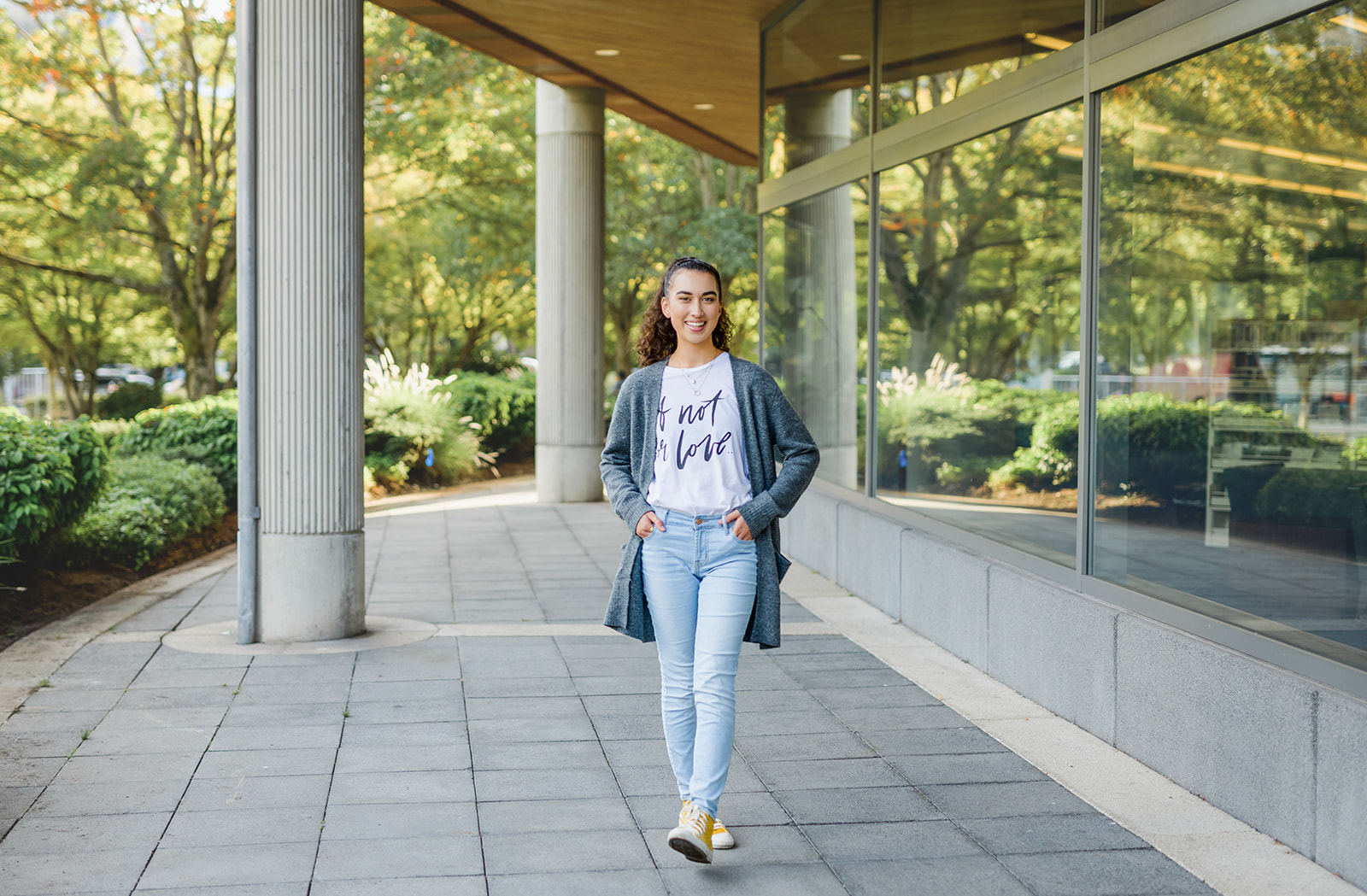 A high school senior walks under a modern designed storefront in jeans and grey sweater and hands in pockets after visiting Colleges Near Seattle