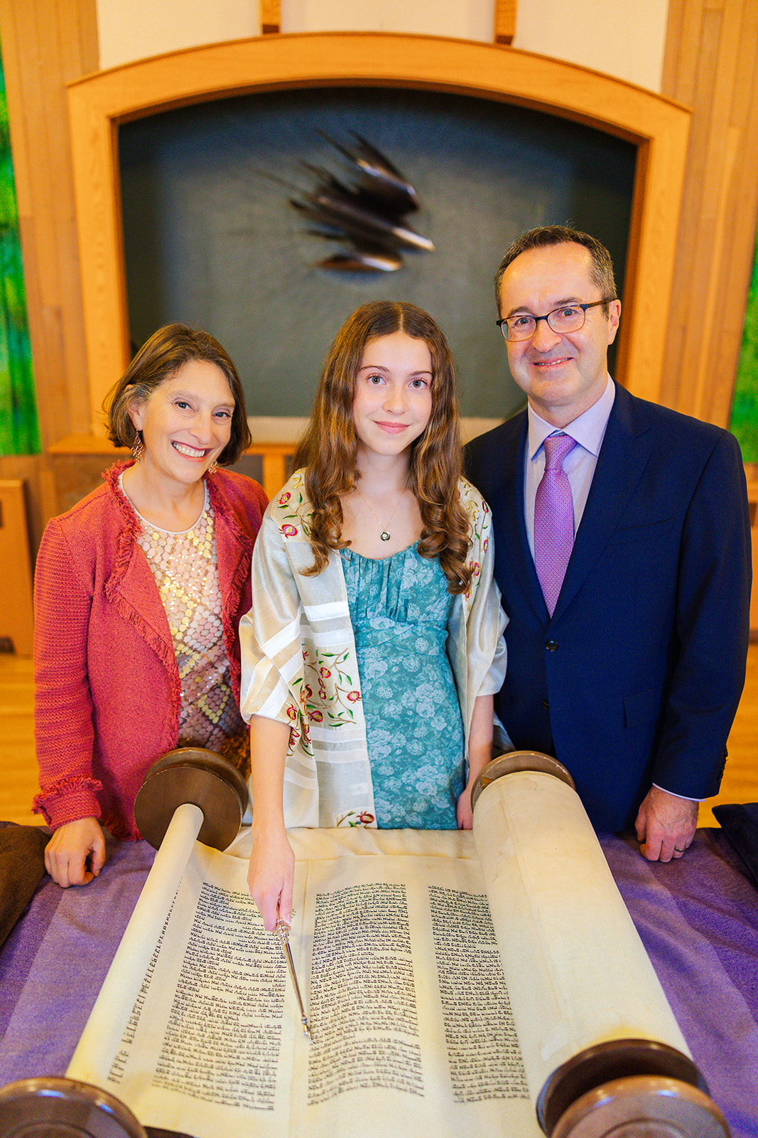 A teenage girl stands at the altar with the Hebrew scroll with mom and dad after her bat mitzvah at Eastside Torah Center