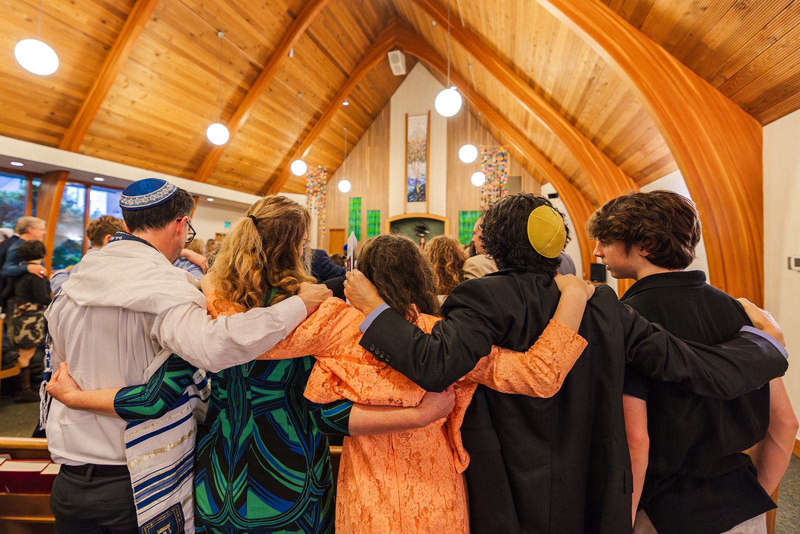 A family stands in the Jewish Community Center Mercer Island during a service with arms around each other