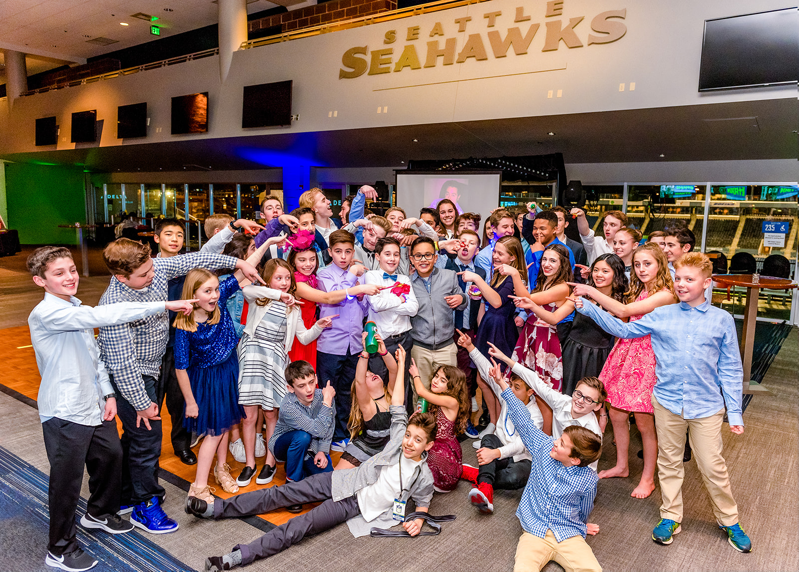 A teen boy stands amongst all his friends as they point to him in the Seahawks stadium after attending Jewish Day School of Metropolitan Seattle