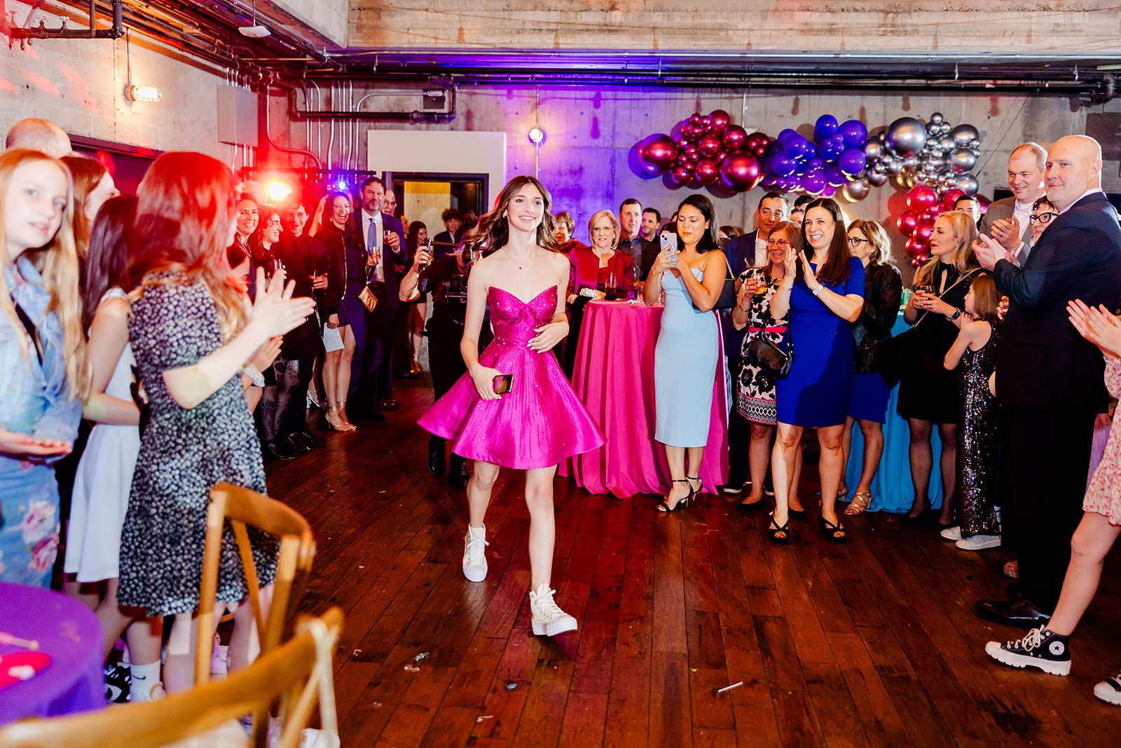 A teen girl in a bright pink dress and sneakers enters her Mitzvah to applause