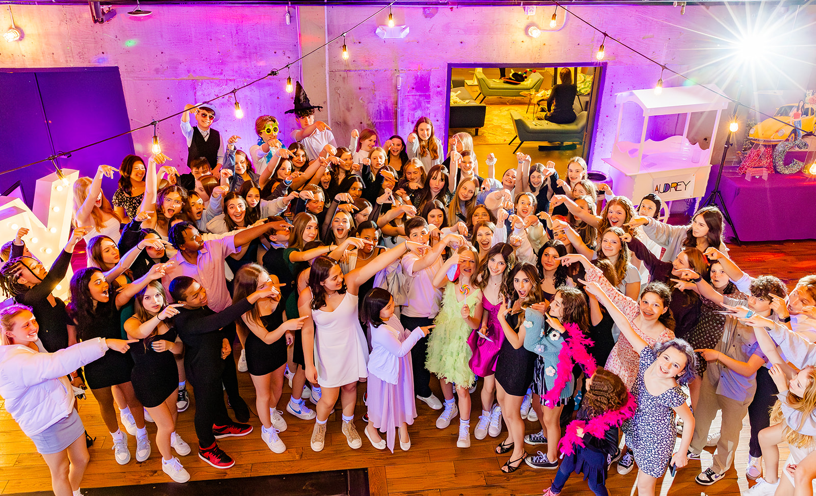 A teen girl in a pink dress stands amongst all her friends as they point at her on the dance floor before visiting Kosher Restaurants Bellevue, Wa