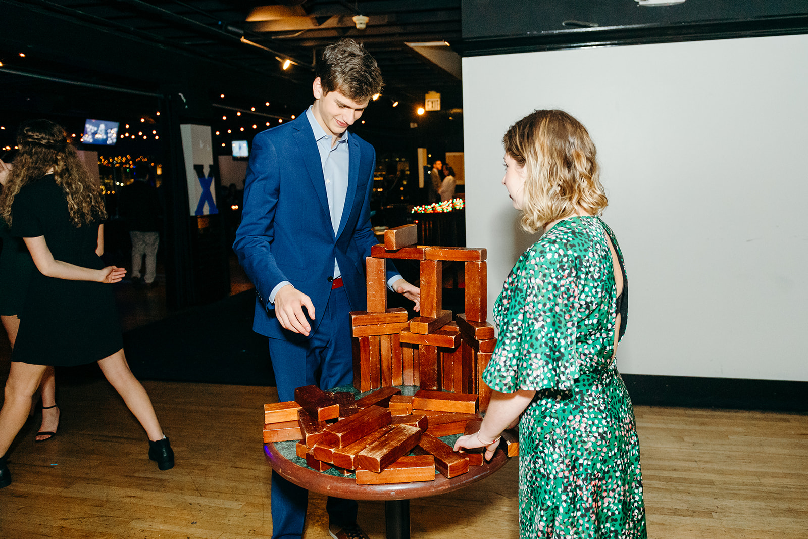 A teen boy in a blue suit and a girl in a green dress play with wooden blocks on a table after attending Seattle Jewish Chorale