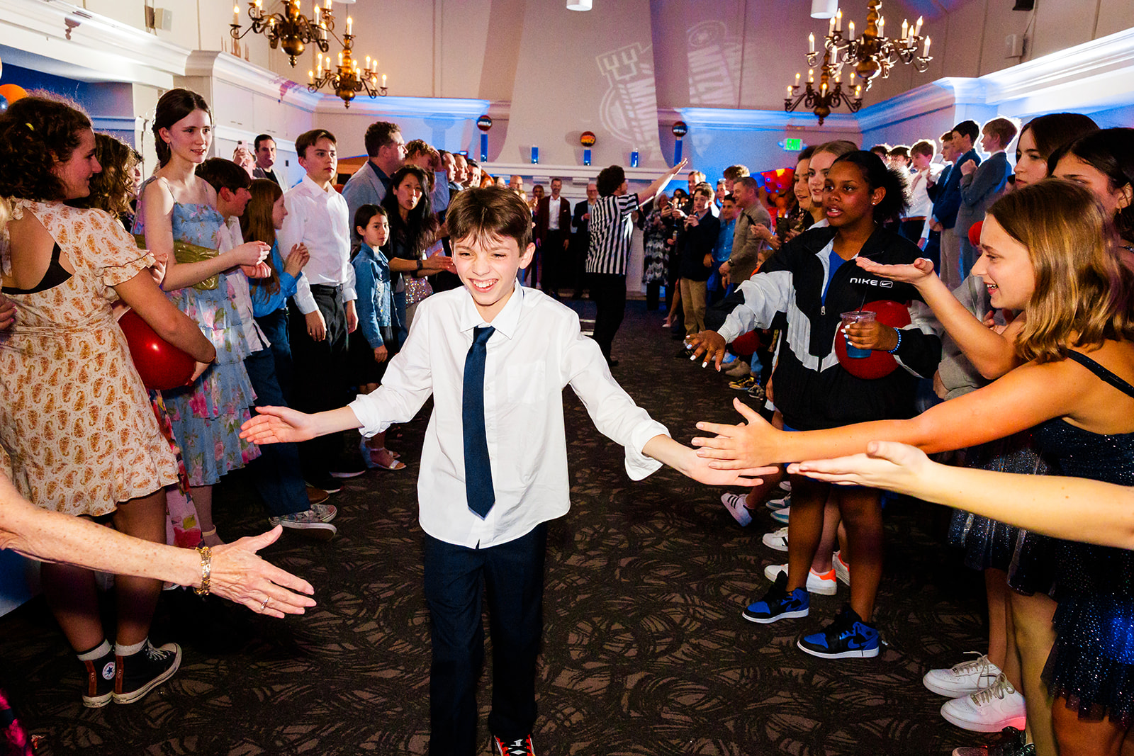 A boy in a button down shirt and tie walks through an aisle of friends giving high fives