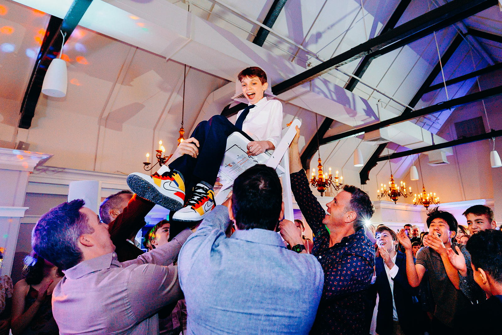 A boy in a suit and Nike's is lifted by the adult men on a chair during his Bat Mitzvah while attending Seattle Jewish Community School