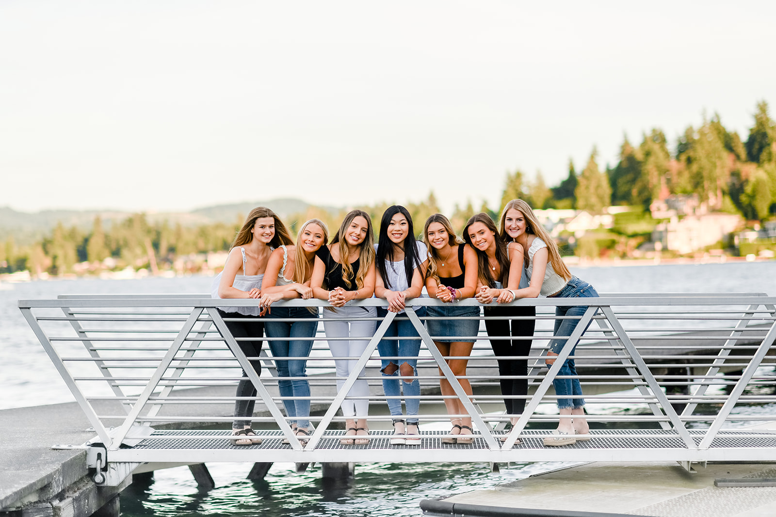 A group of high school senior girls lean on a marina railing at sunset after attending Bellevue high school Washington