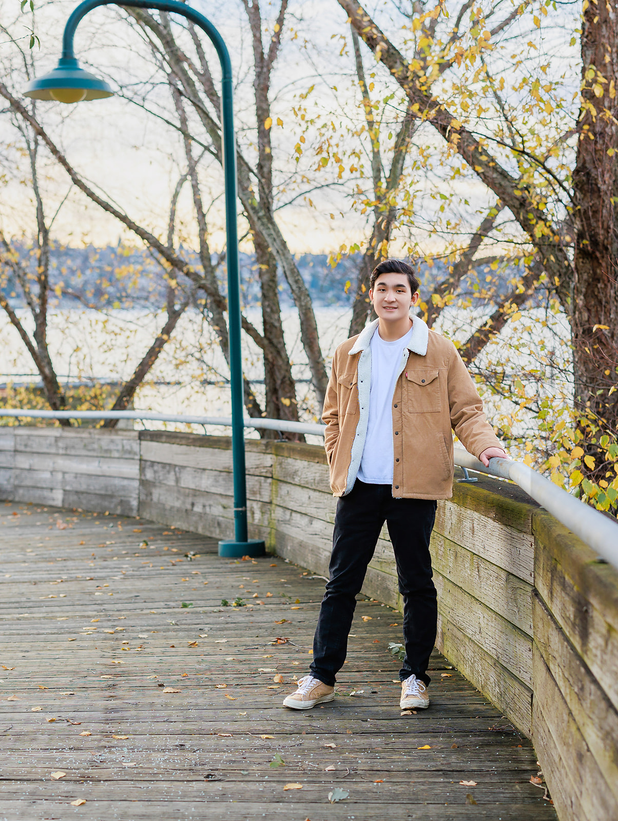 A high school senior stands on a boardwalk in a thick jacket in fall after attending Bellevue high school Washington