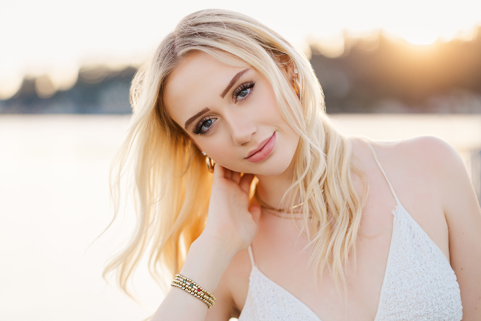 A high school senior walks on a windy beach at sunset in a white dress after using Makeup Artists Bellevue