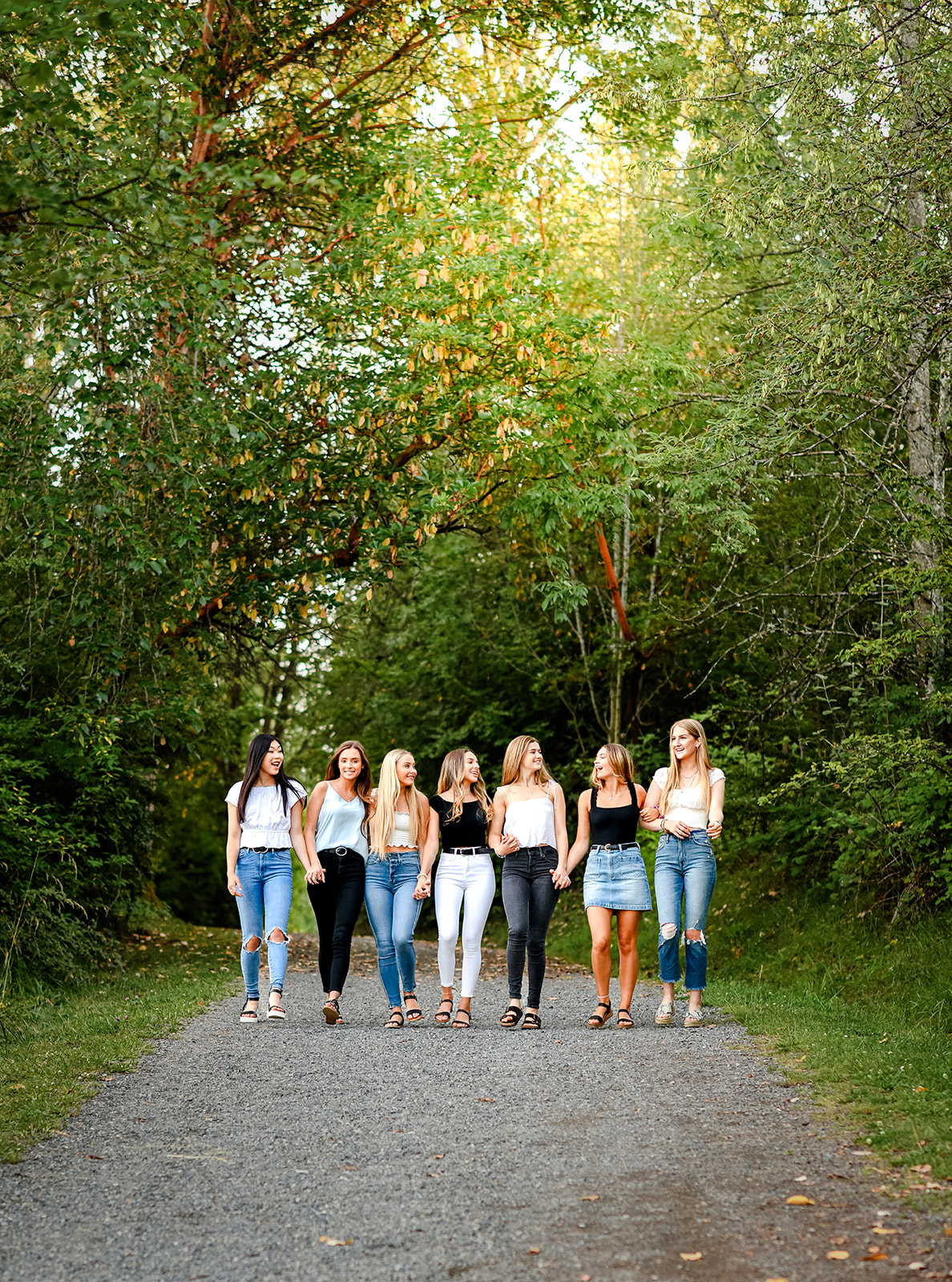 7 teenage girls from Mercer Island High School hold hands while walking through a park path during a photo shoot