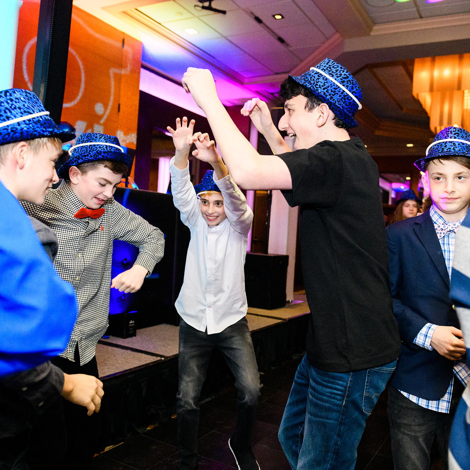 A group of boys in suits and blue hats dance on the dance floor