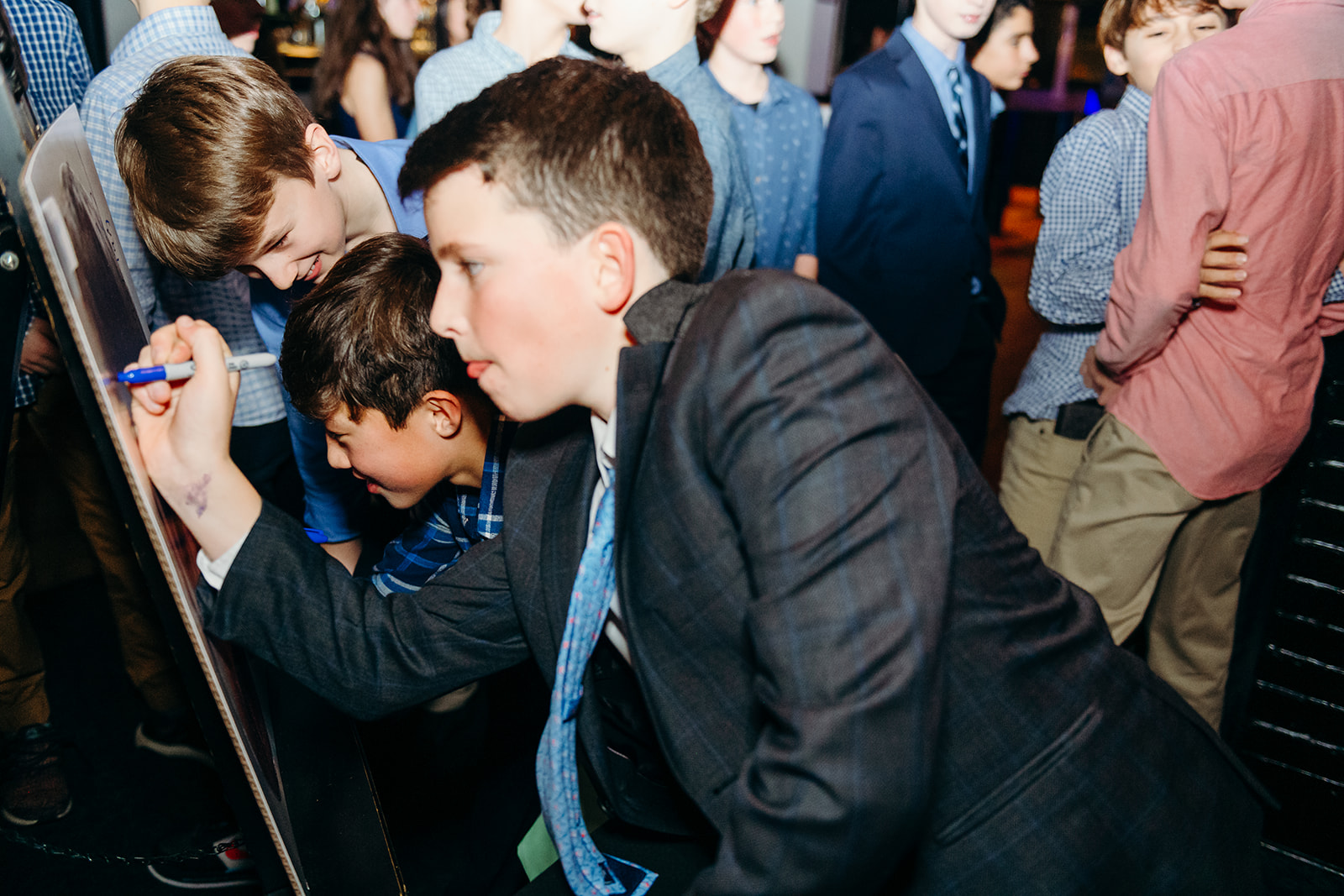 Some boys in suits sign a board at a Mitzvah