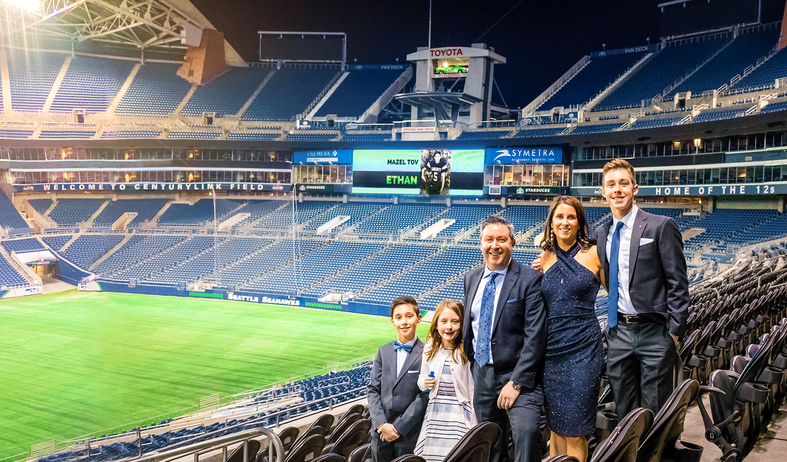 A family of 5 stand in a football stadium with arms around each other in blue suits and dresses for a boy's Mitzvah at one of the Mitzvah Venues Seattle