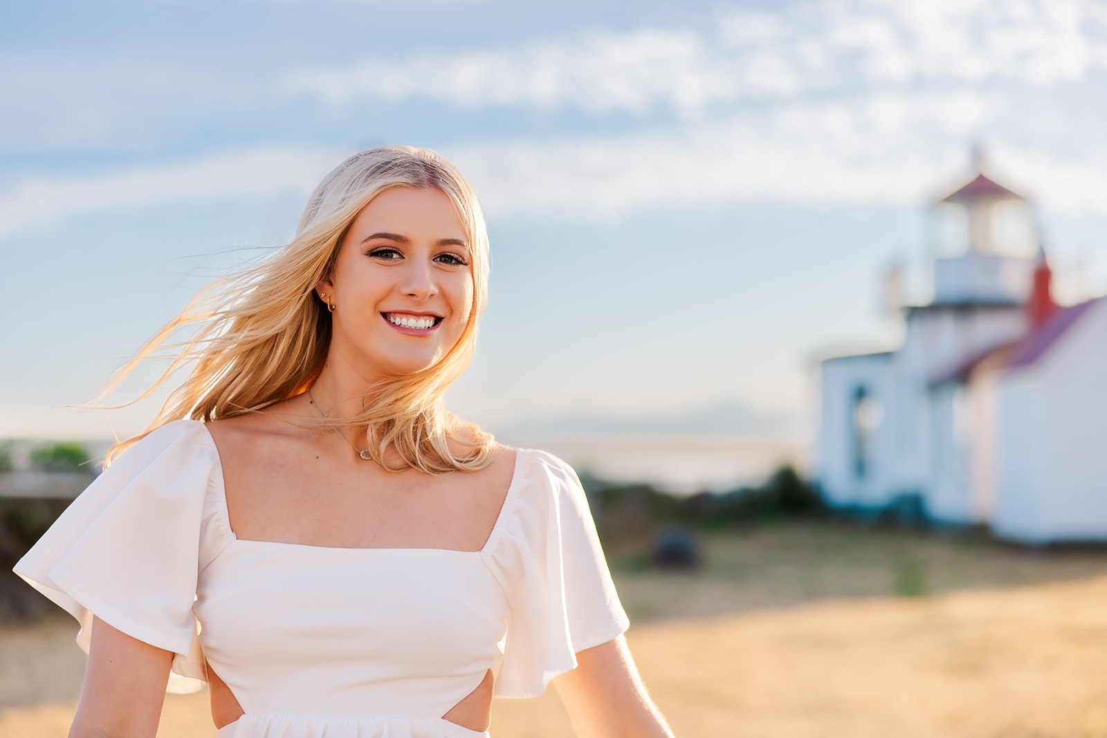 A high school senior in a white dress smiles while walking in a park at sunset after visiting Nail Salons Bellevue