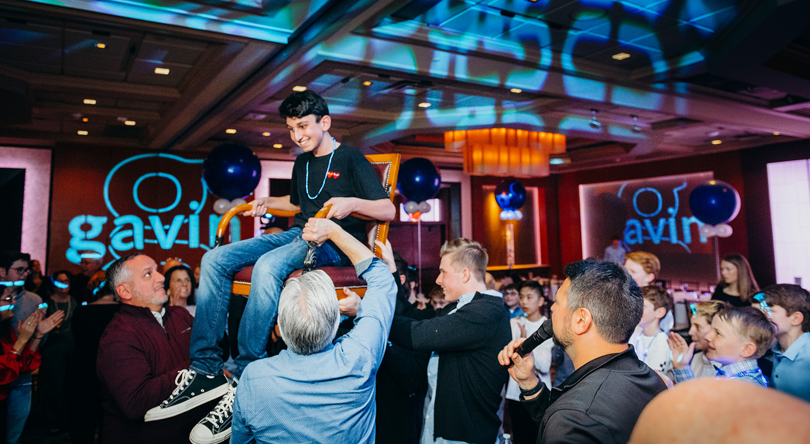 A teen boy is lifted in a chair on the dance floor surrounded by friends and family at his bar mitzvah that has a Photobooth Rental Bellevue