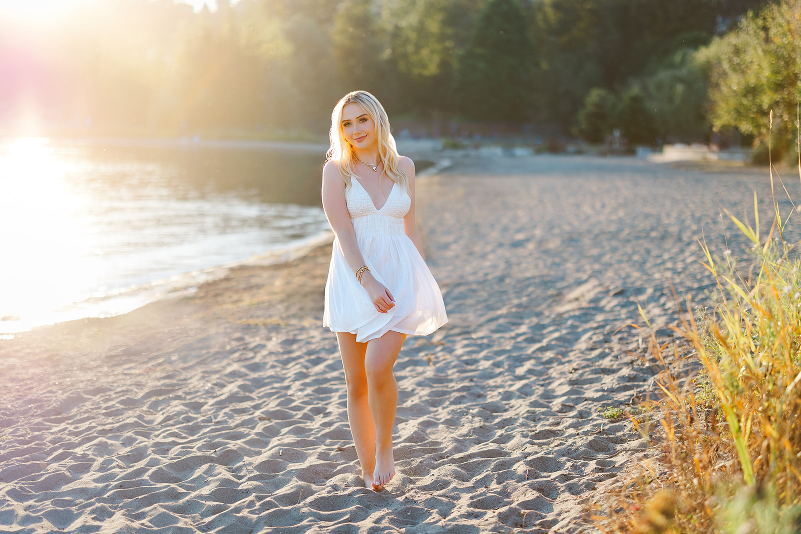 A high school senior walks up a beach at sunset in a white dress