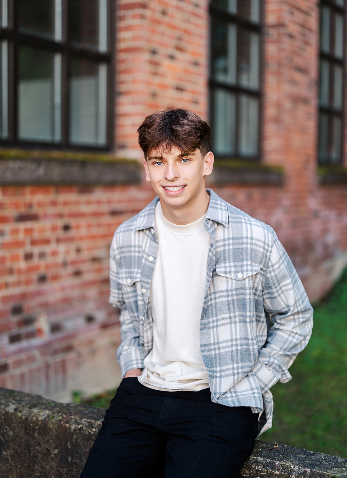 A high school senior in a plaid shirt and black pants sits on a concrete wall with hands in his pockets after some SAT Prep Bellevue