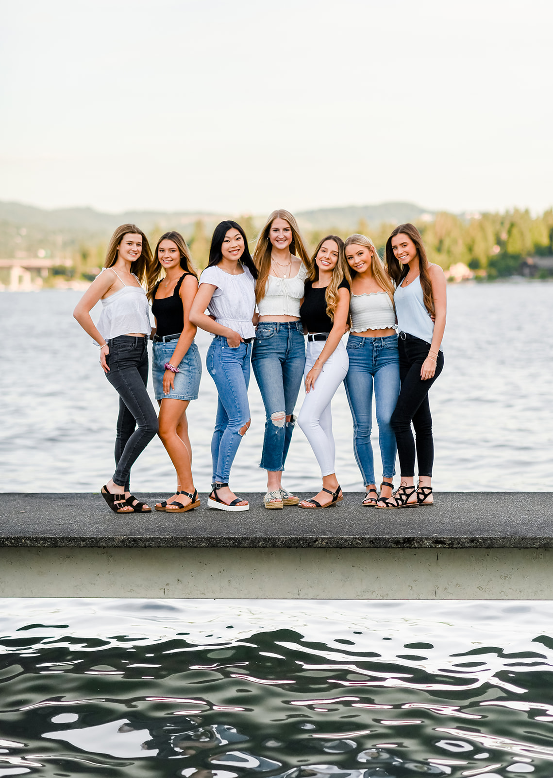 A group of high school girlfriends stand together on a dock in jeans and shirts after visiting Tanning Salons in Bellevue