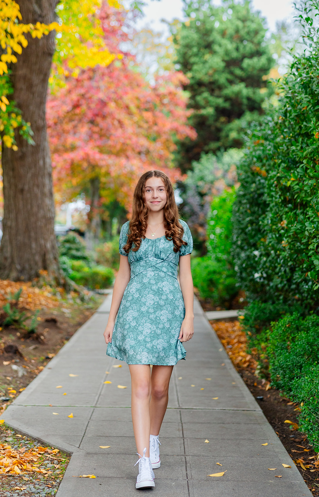 A teenage girl in a blue dress walks through a fall park sidewalk before her bat mitzvah at Temple B'nai Torah