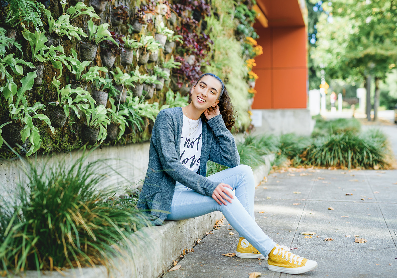 A high school senior in jeans and yellow converse sits on a park garden barrier after some Tutoring in Bellevue