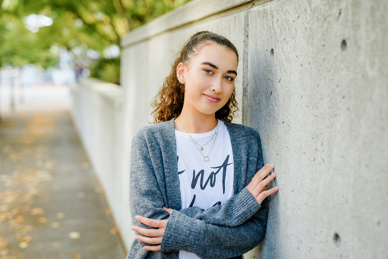 A high school senior girl leans against a cement wall in a park in a grey sweater before some Tutoring in Bellevue