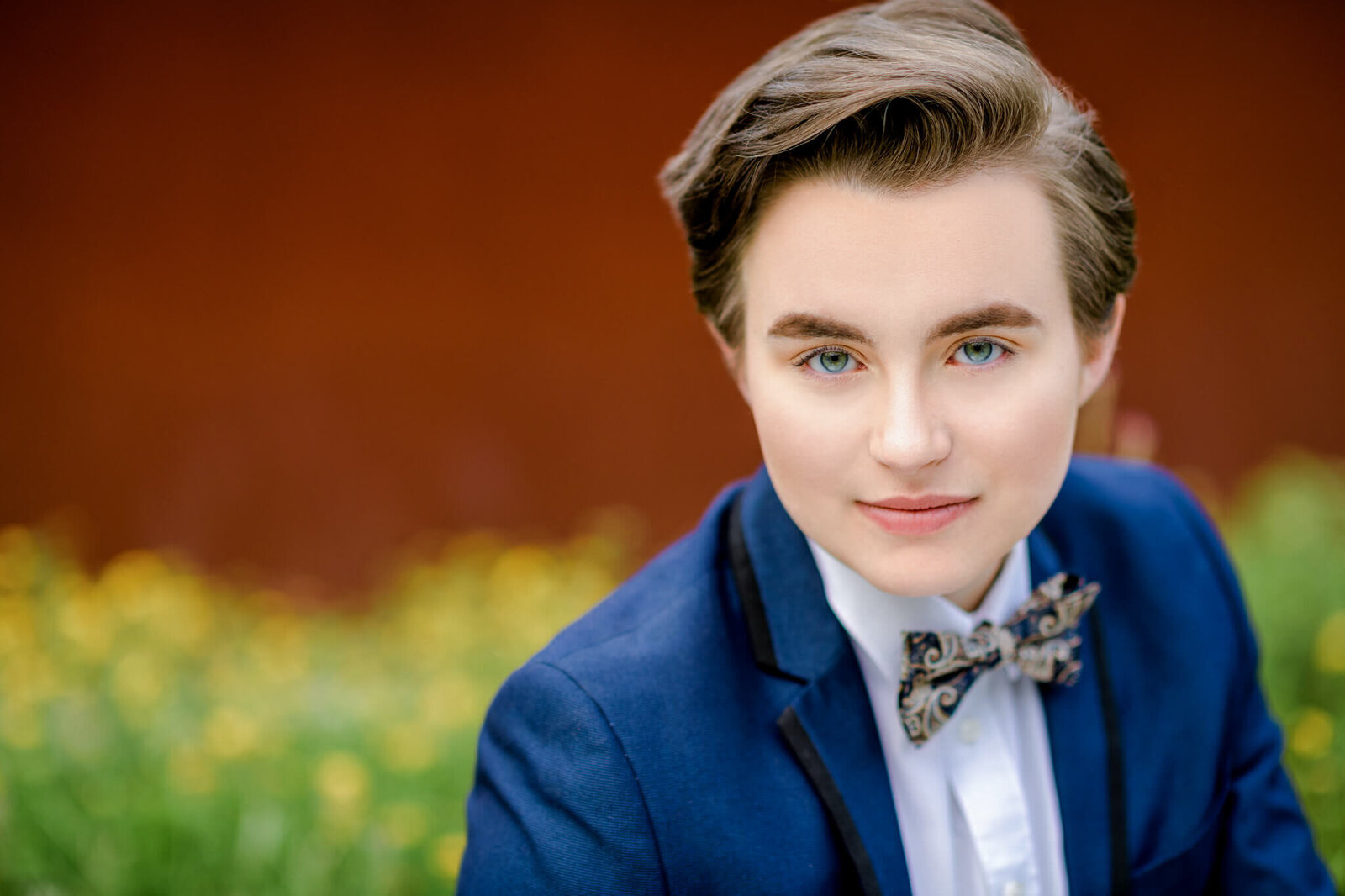 A teen with blue eyes sits in a garden in a blue and black tuxedo from a tux shop bellevue