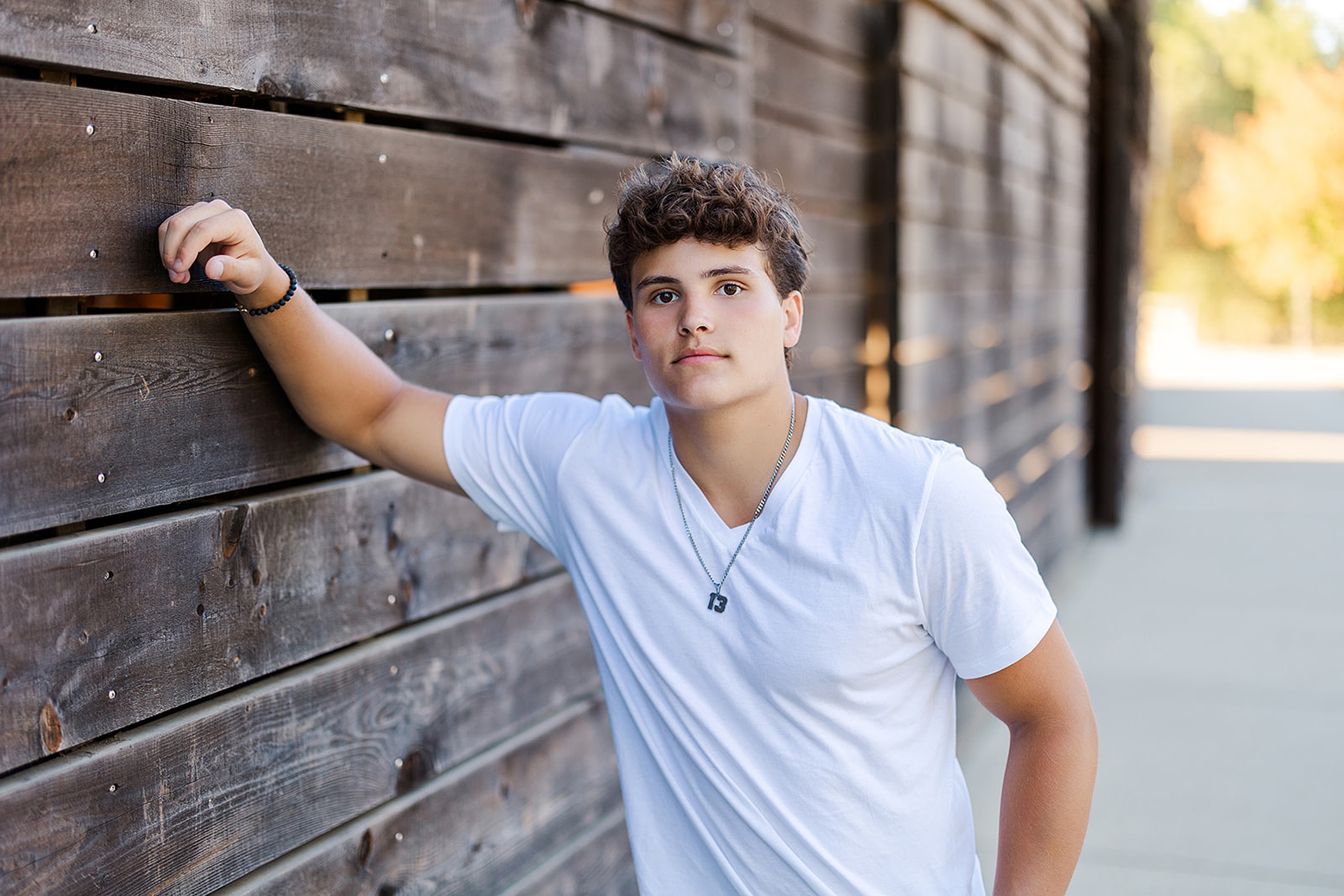 A high school senior in a white shirt leans on a rustic wood wall in a park at sunset after finding SAT Prep Mercer Island