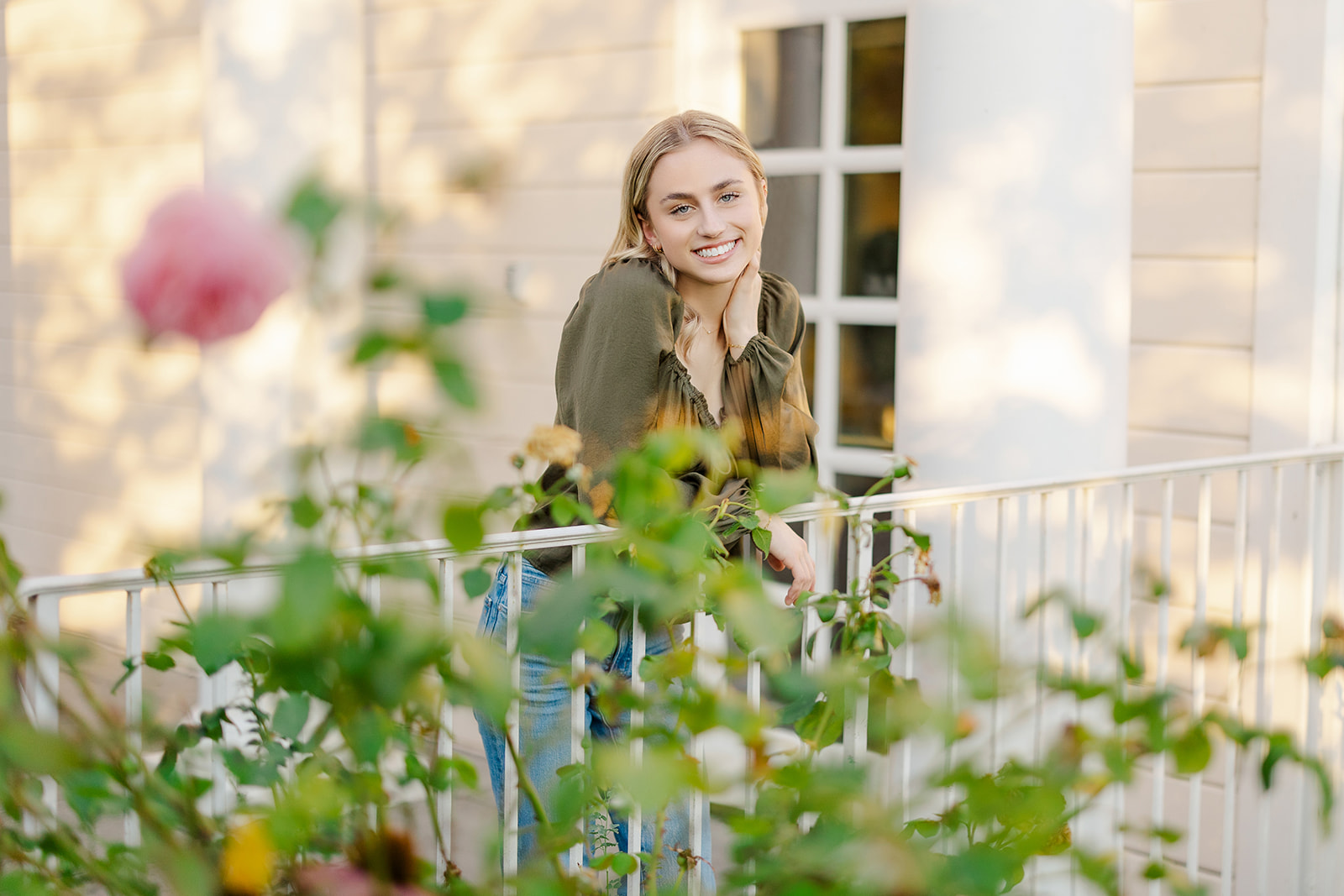 A high school senior leans on a white railing overlooking a rose garden