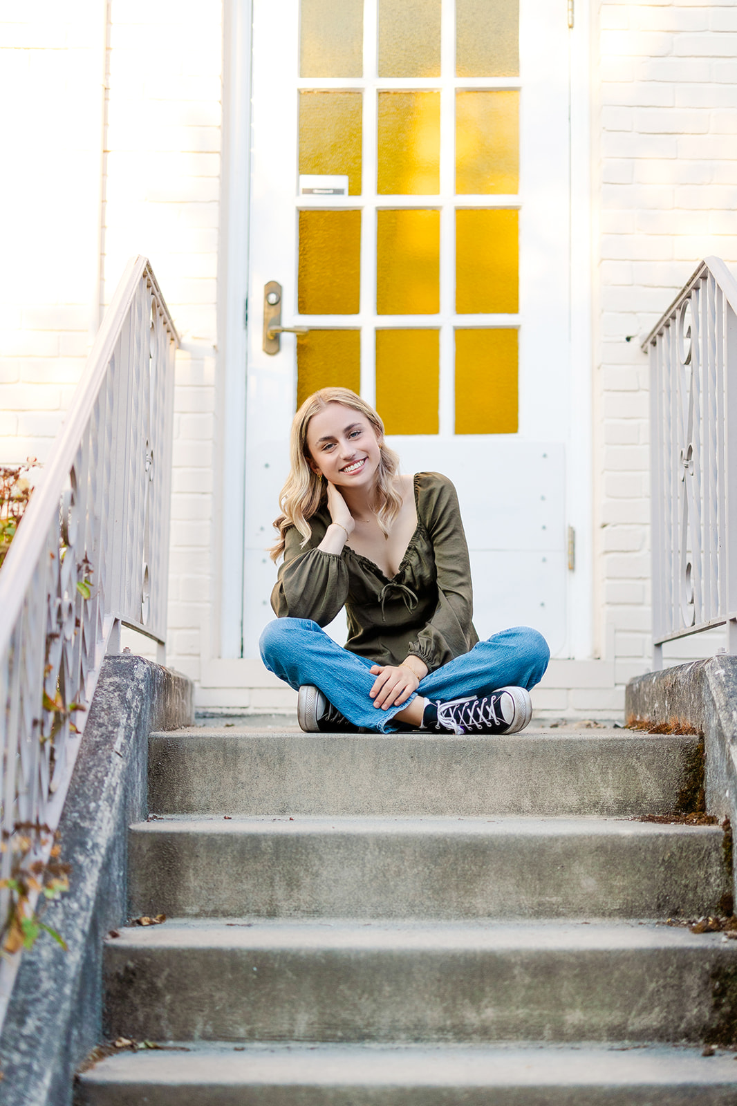 A High school senior sits crossed legged on a stoop in jeans and a green top after visiting Mercer Island Hair Salons