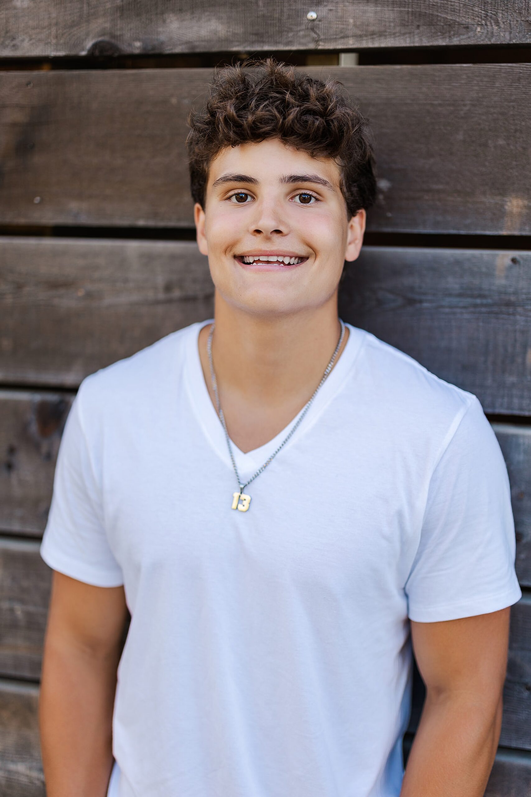 A high school senior in a white shirt smiles while leaning against a rustic fence after attending Mercer Island Private Schools