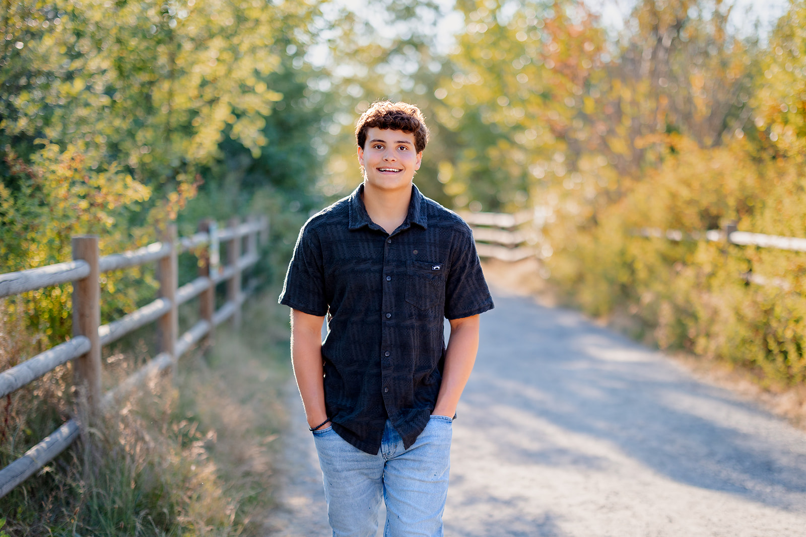 A high school senior walks down a park path at sunset smiling with hands in his jean pockets after visiting Mercer Island Synagogue