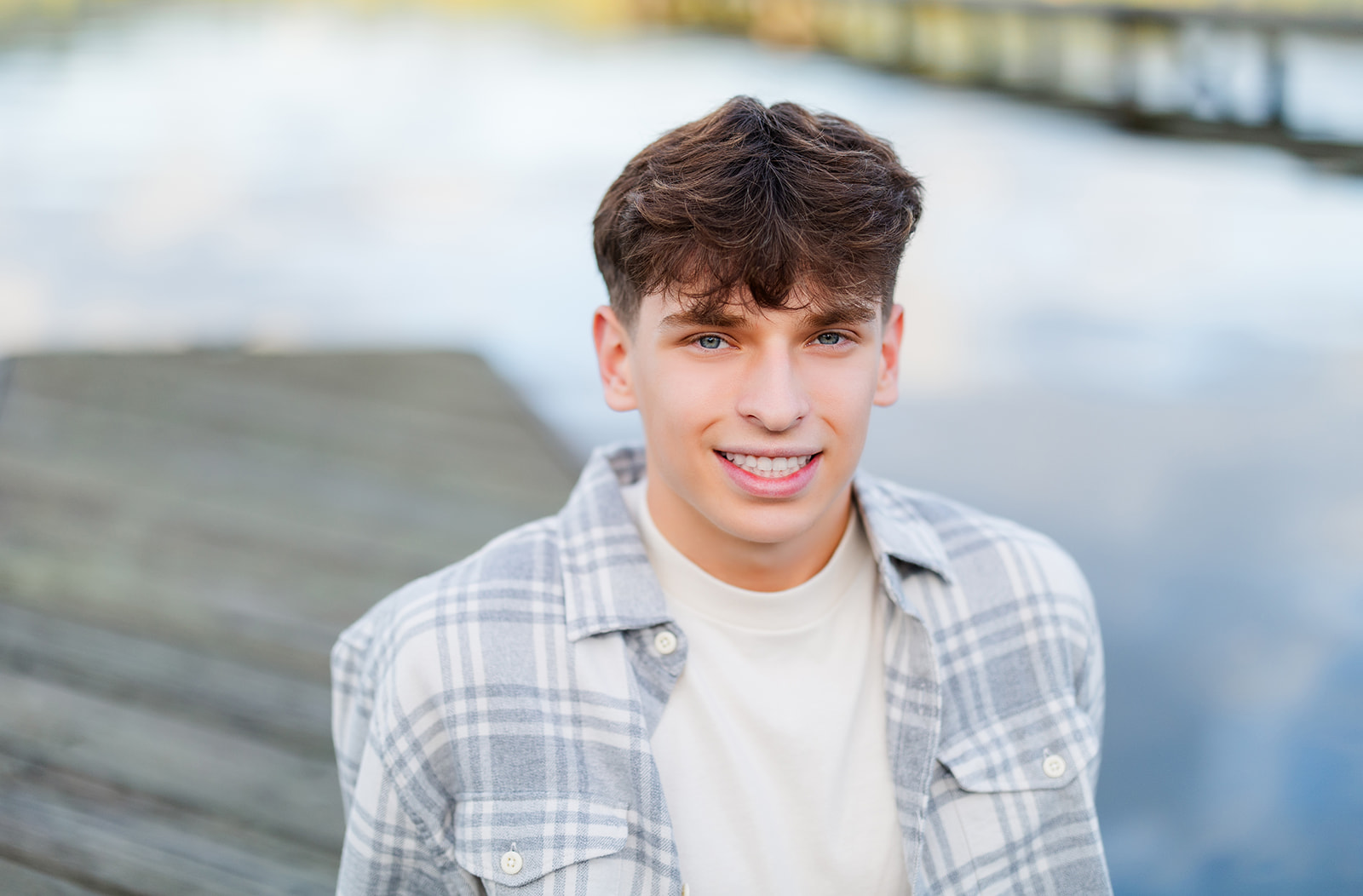 A close up shot of a high school senior sitting on a dock smiling