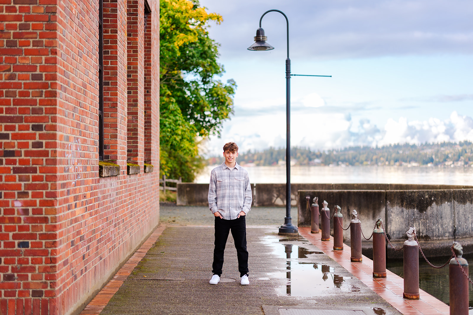 A high school senior stands in a riverside alley by a red brick building with hands in his pockets after attending Torah Day School Of Seattle