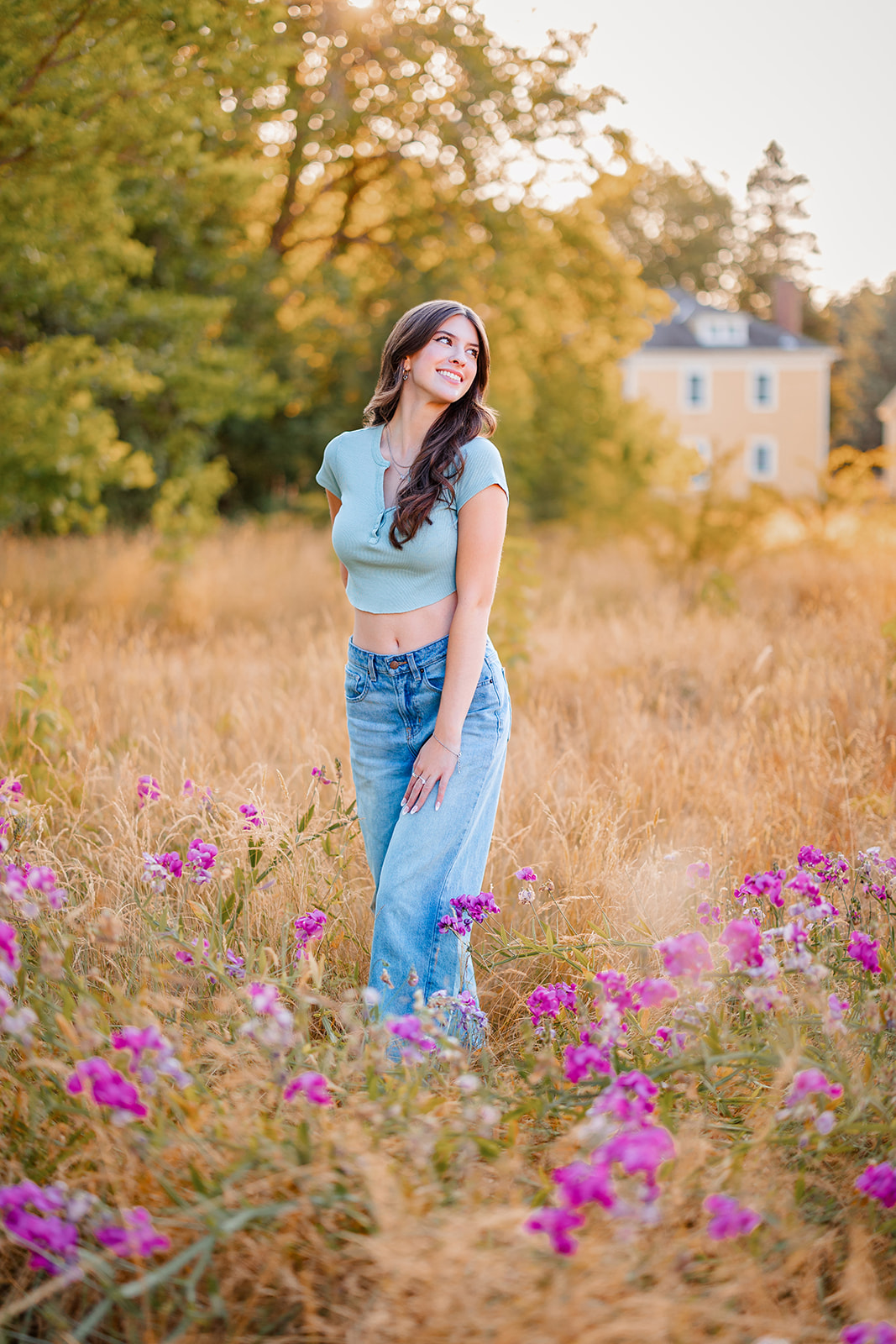 A high school senior in jeans and a blue shirt walks through a field of wildflowers and golden grass at sunset after attending Bellevue Private Schools