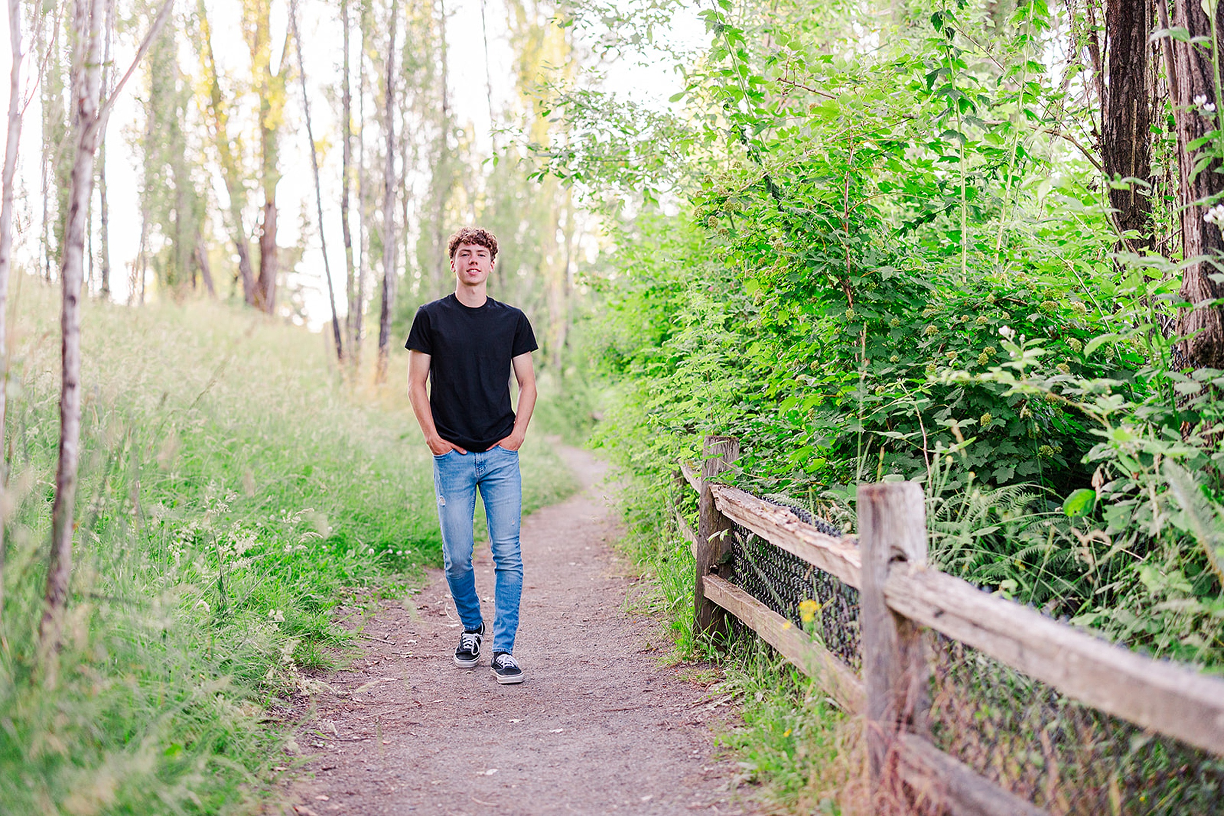 A teenage boy walks down a forest trail with hands in his pockets in a black shirt