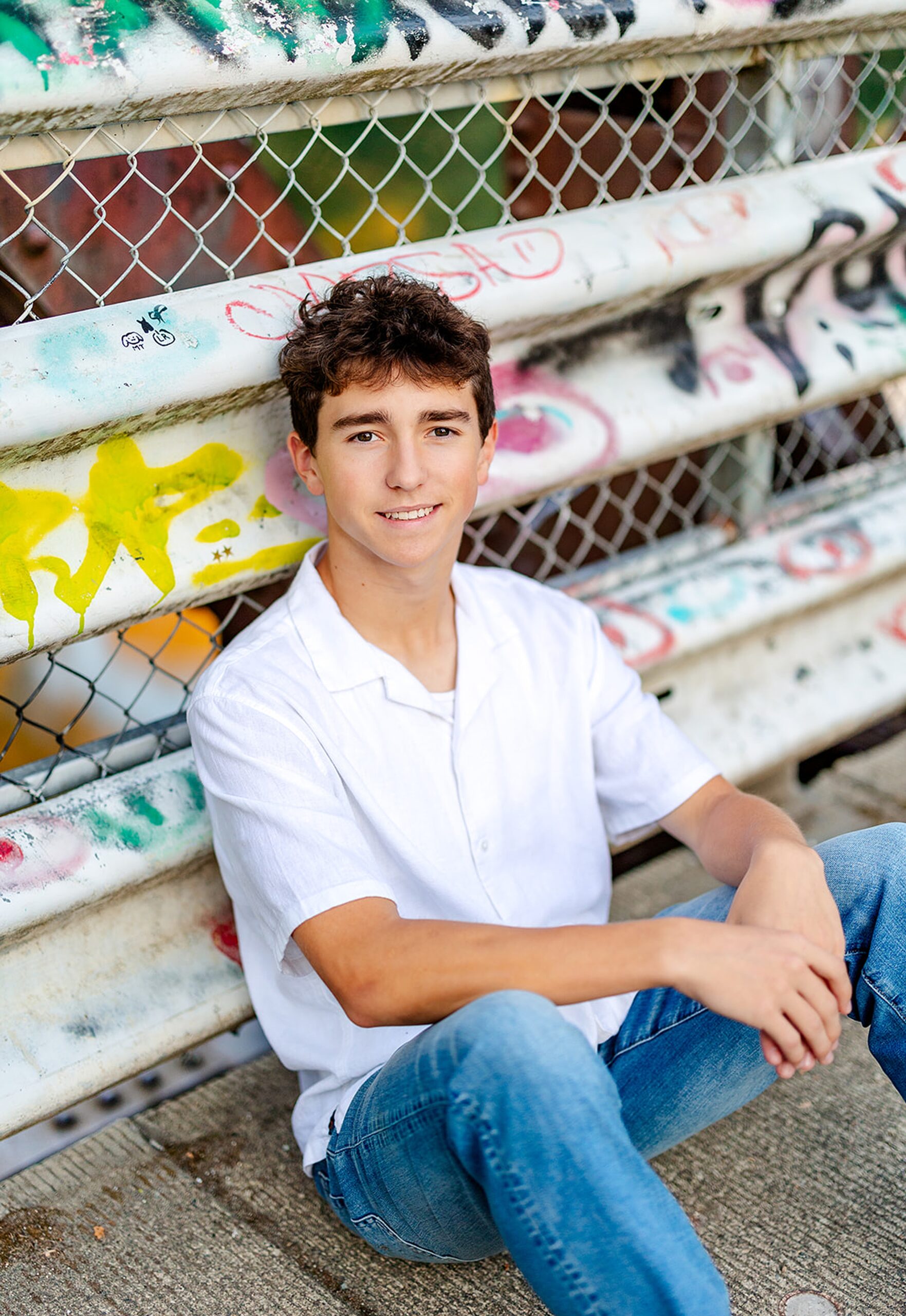 A teenage boy sits against a graffiti covered bridge railing before visiting Colleges Near Kirkland, WA