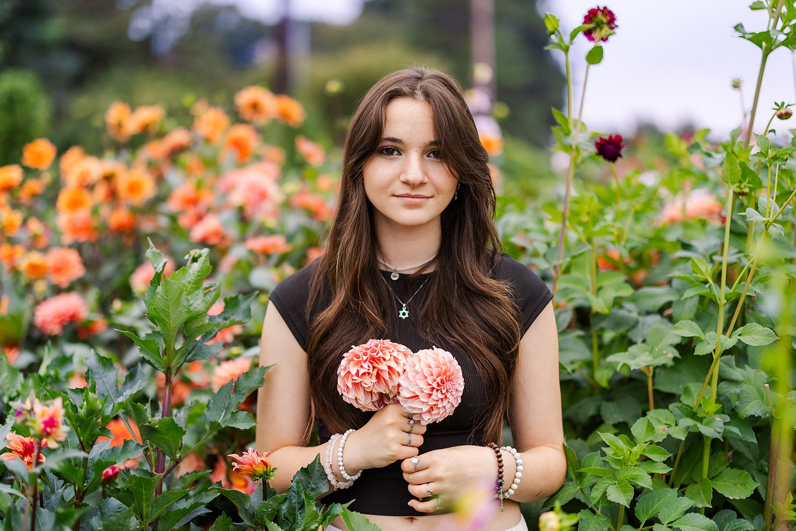 A teenage girl in a black shirt stands in a colorful flower garden while holding pink flowers before visiting Florists Kirkland, WA