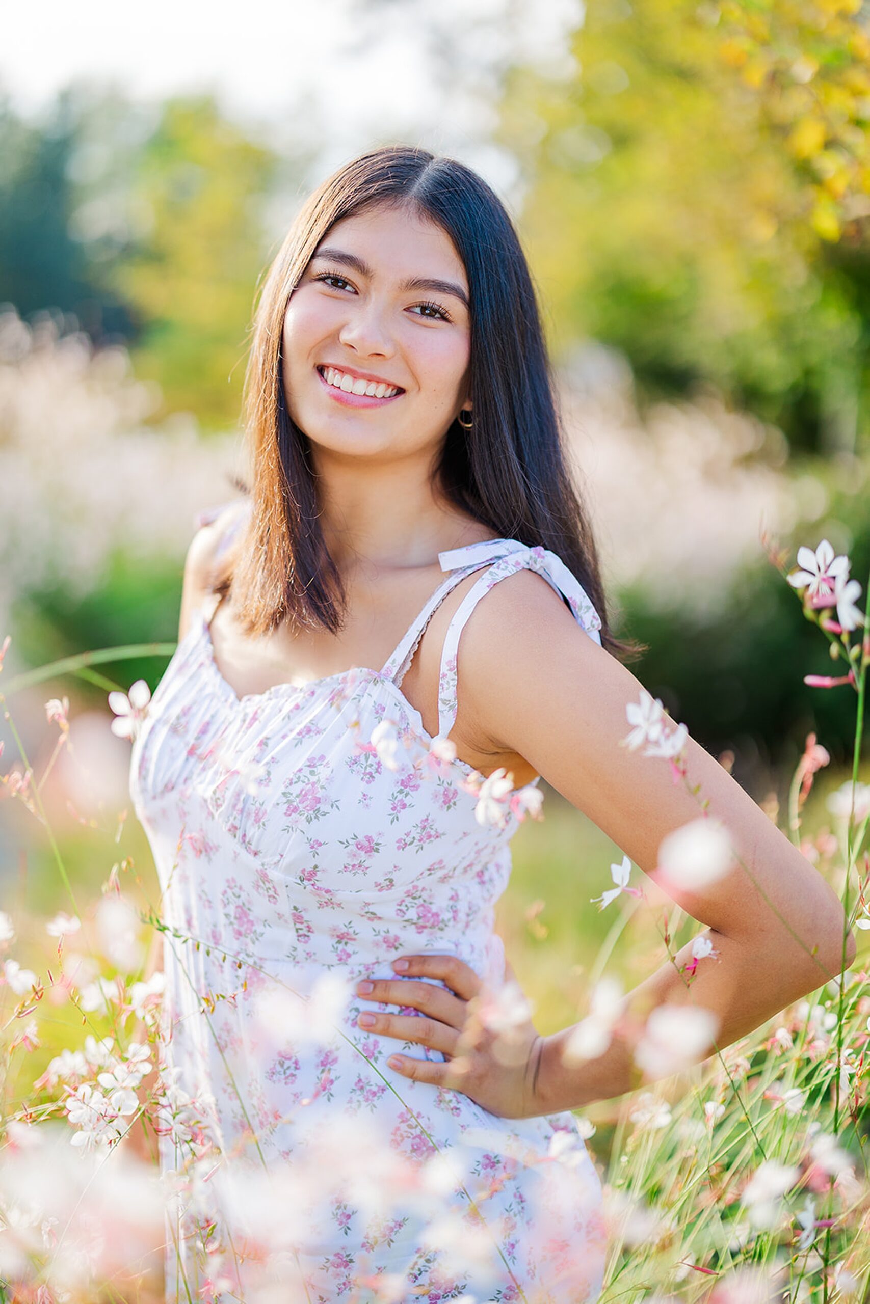 A proud senior in high school in a white and pink dress wanders through a garden of pink and white flowers