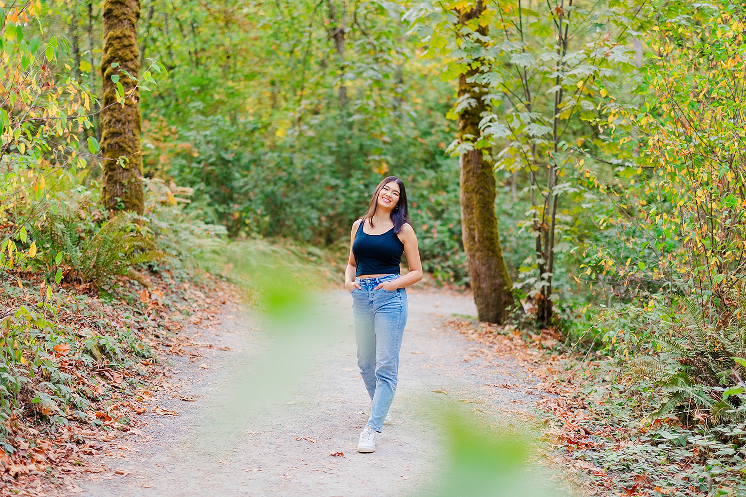 A high school senior walks through a park forest trail with hands in her jean pockets after visiting Issaquah Boutiques