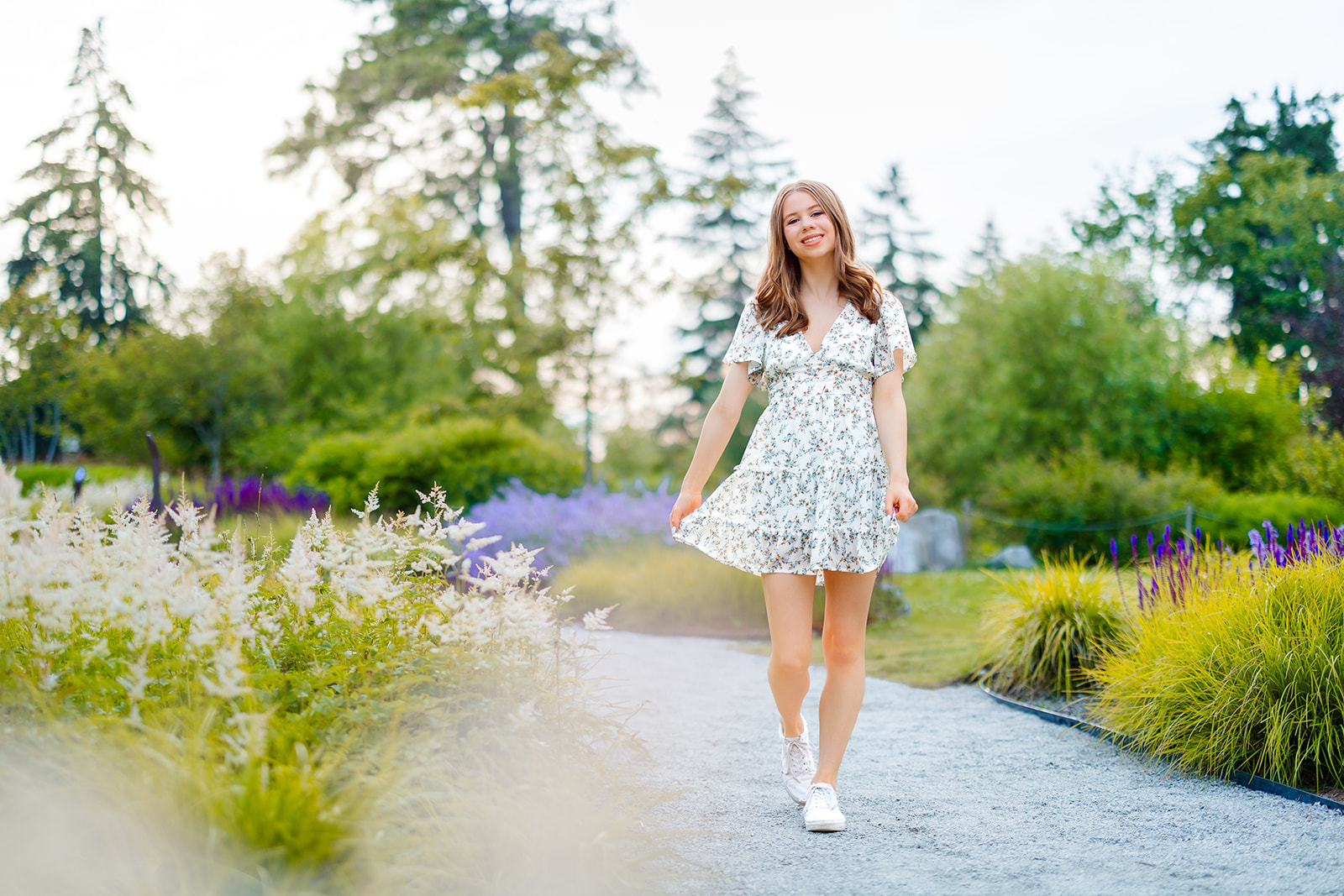 A high school senior in a floral print sun dress walks through a garden trail at sunset before visiting Issaquah Florists