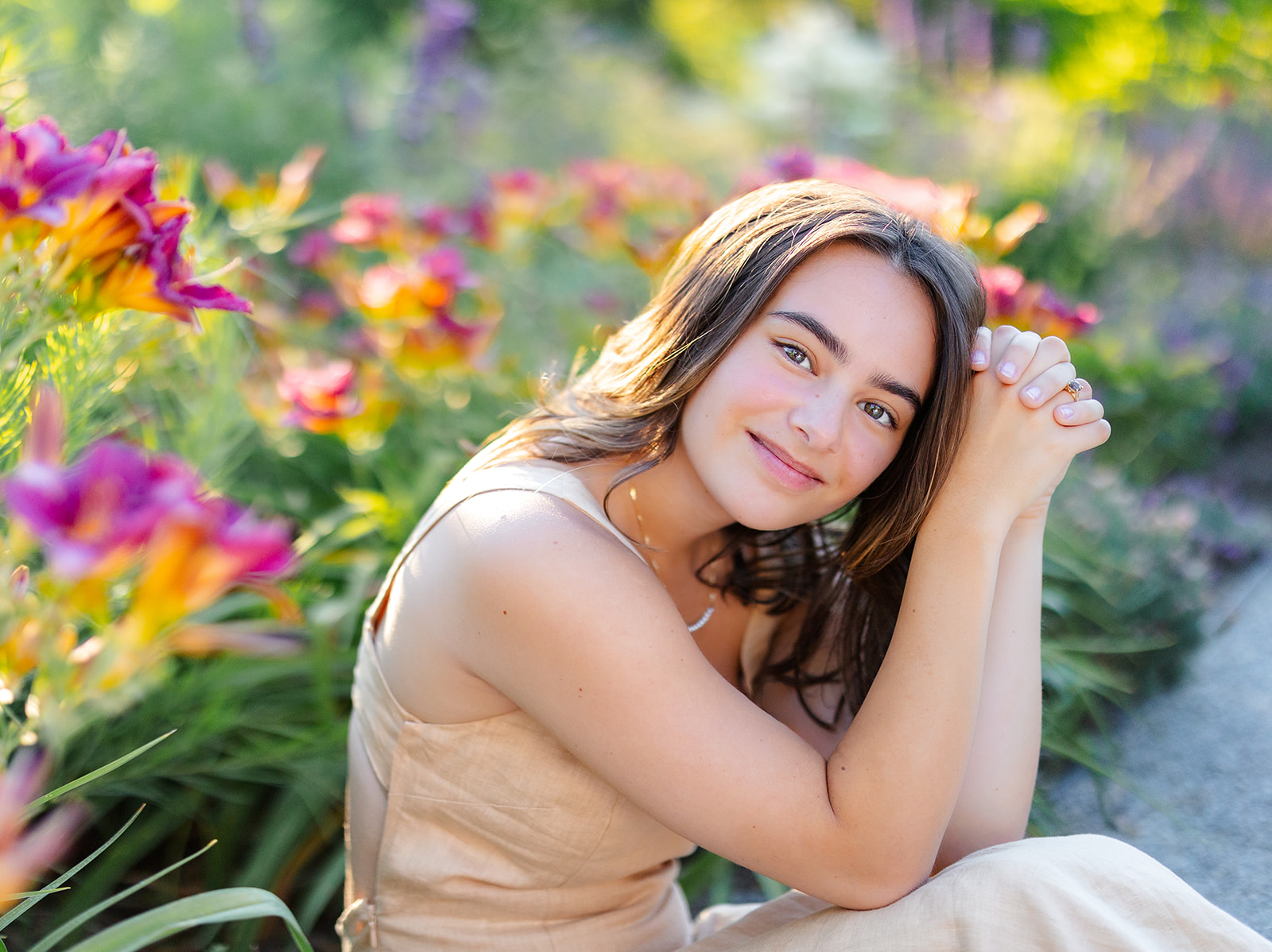 A high school senior in a tan dress sits in a colorful garden after visiting Issaquah Hair Salons