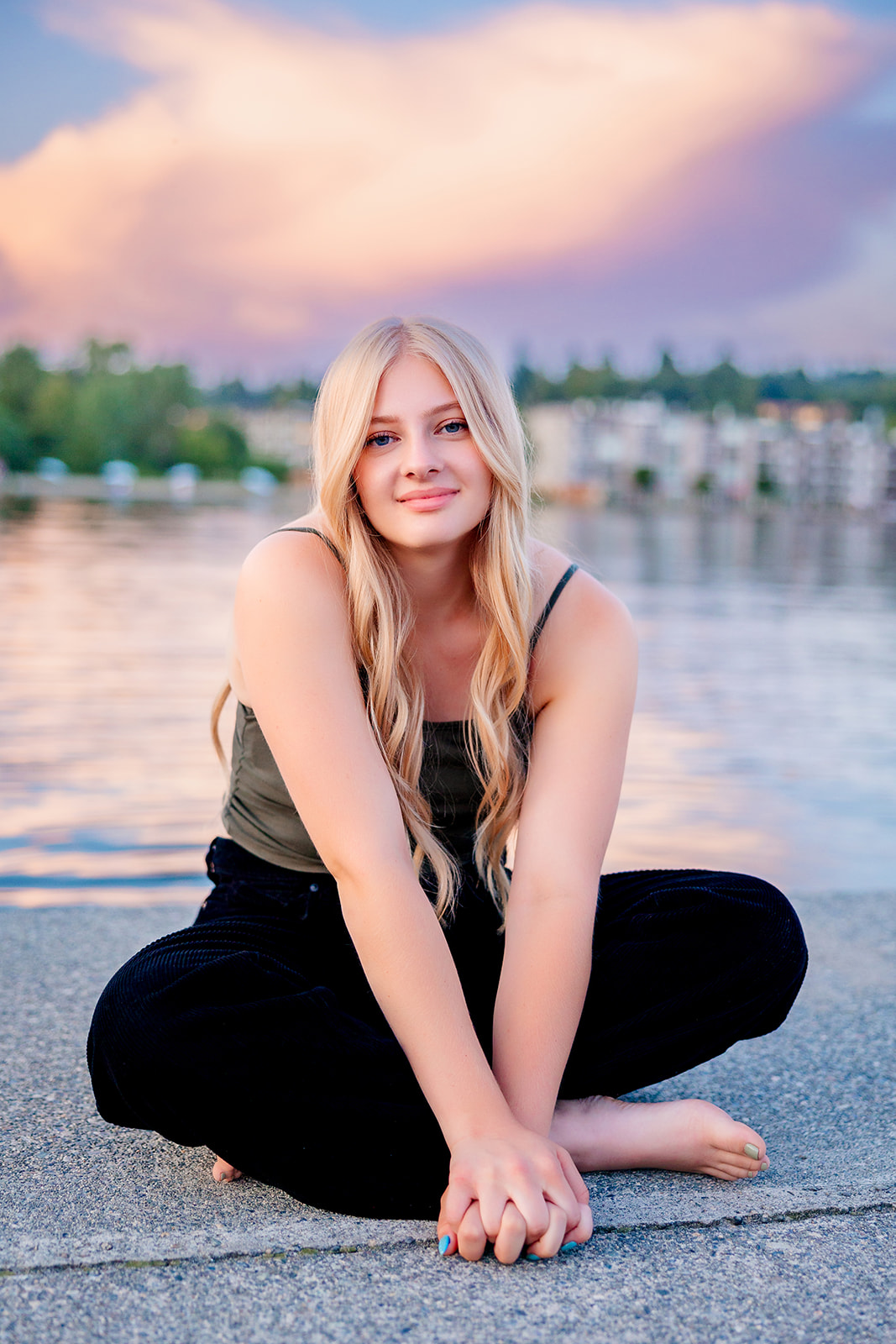 A blonde high school senior sits on a dock with legs crossed after visiting Issaquah Tanning Salons