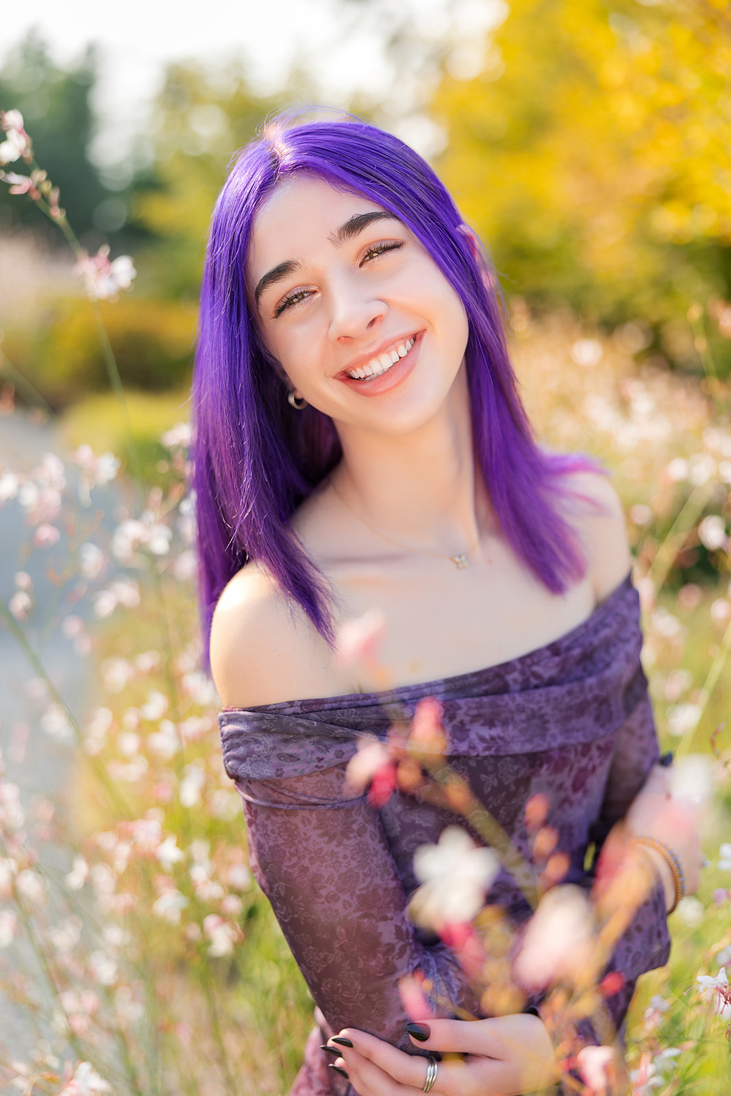 A teenage girl with bright purple hair smiles while standing in a garden at sunset after using Kirkland Nail Salons