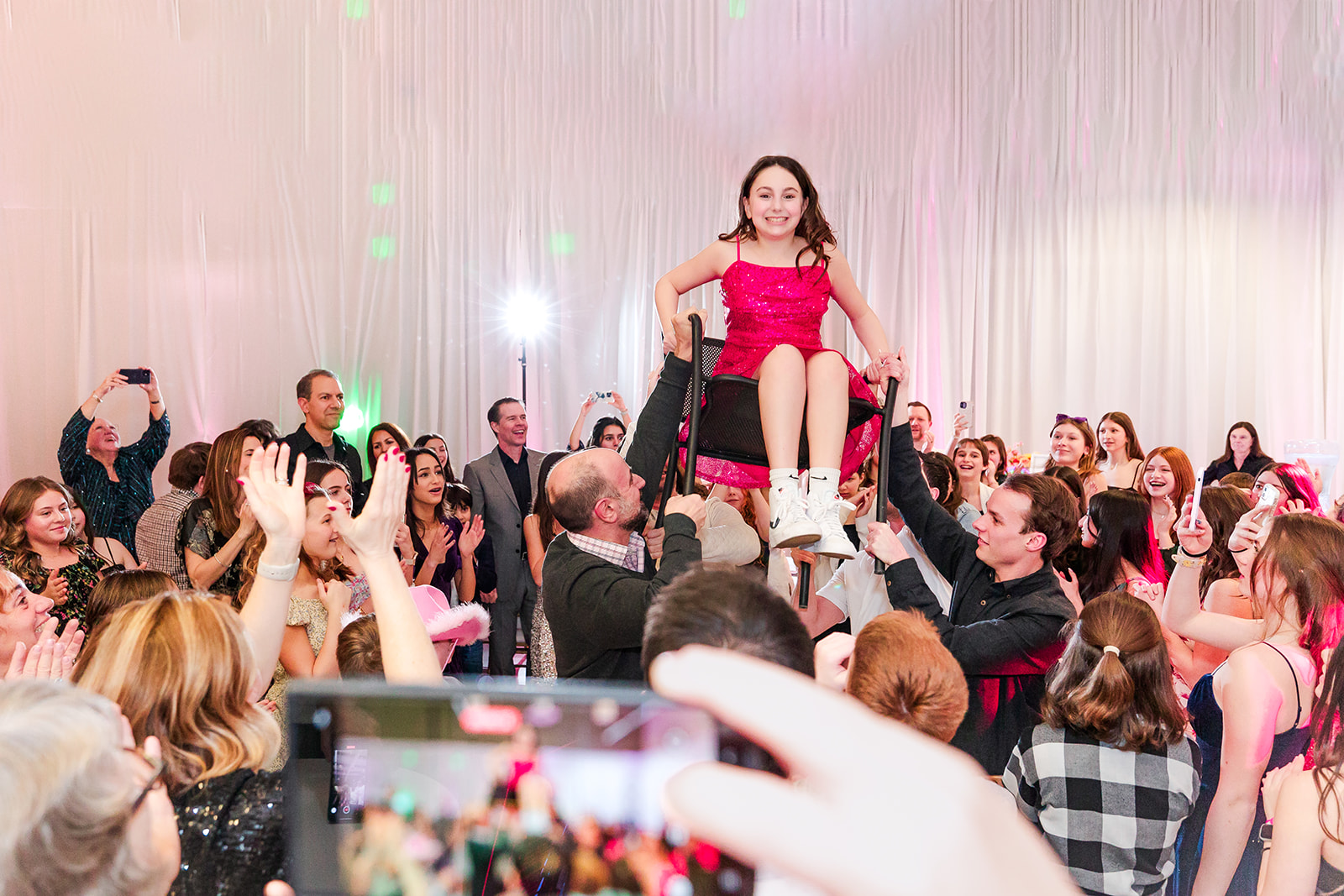 A young girl in a pink dress sits in a chair being lifted on the dance floor during her mitzvah celebration at one of the Kirkland party venues