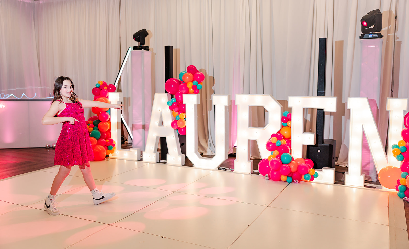 A young teen in a pink dress points at her name in light boxes on the dance floor of one of the Kirkland party venues