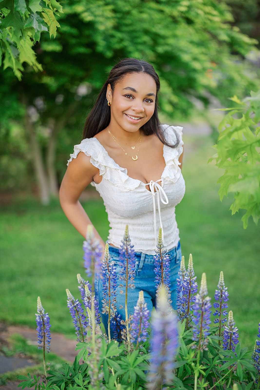 A high school senior in a white blouse stands in a garden of flowers with hands in her back pockets before exploring Mercer Island Boutiques