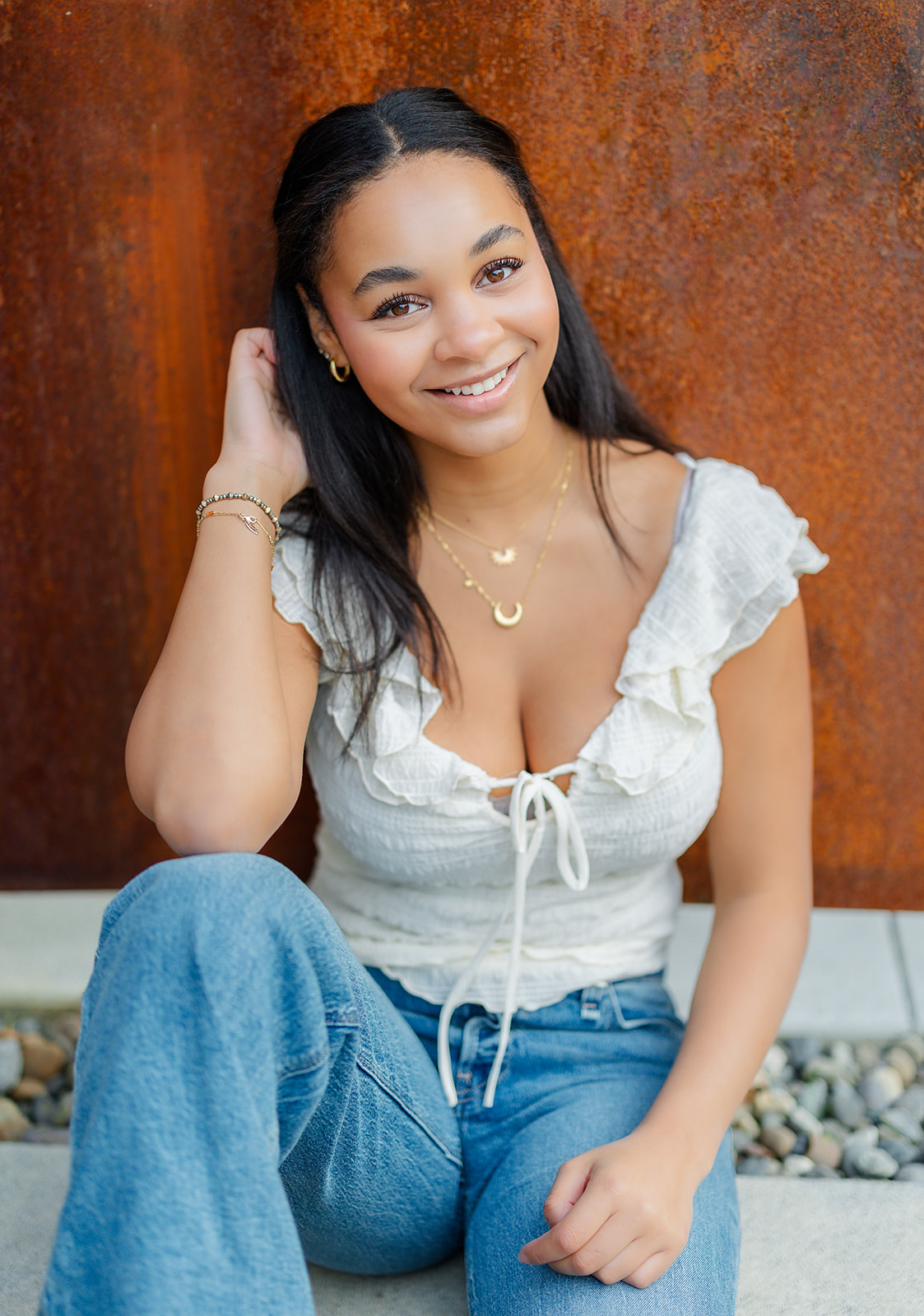 A teenage girl in jeans and a white top leans against a rusted wall while sitting after exploring Mercer Island Boutiques