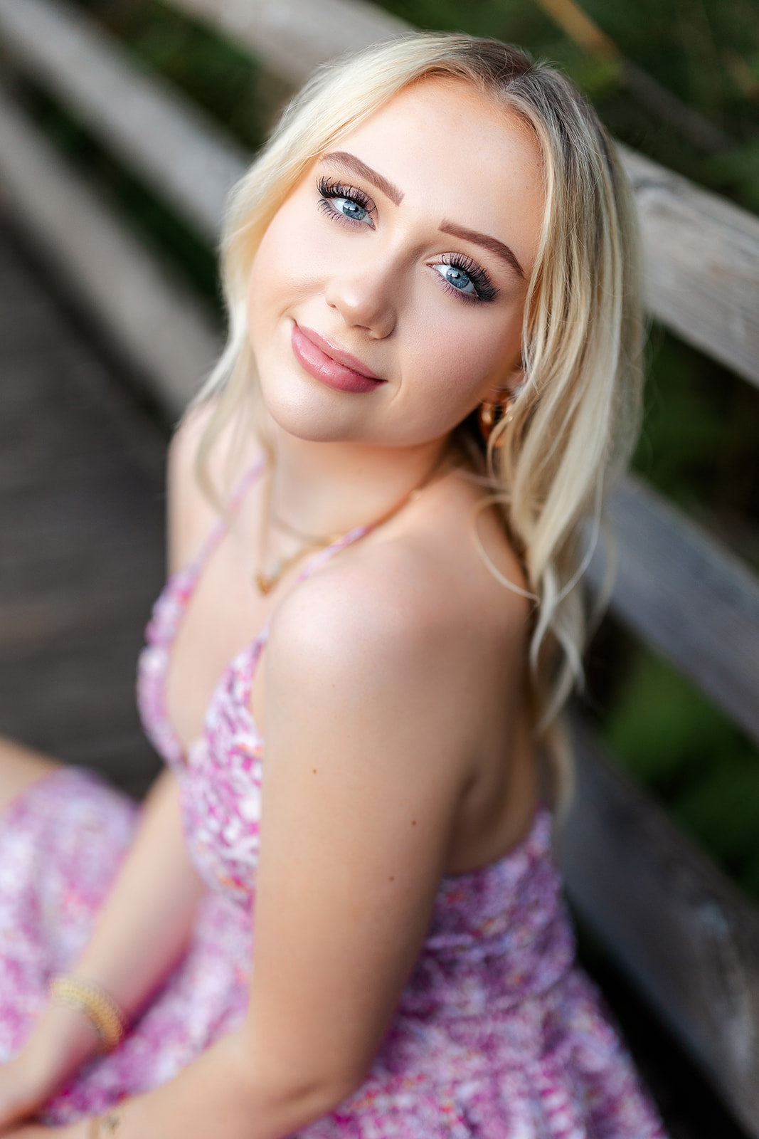 A blonde high school senior sits on a wooden bridge in a pink dress before shopping for Prom Dress Bellevue