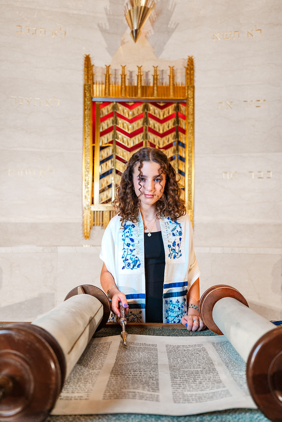 A young woman reads from the torah with the pointer in am embroidered traditional covering